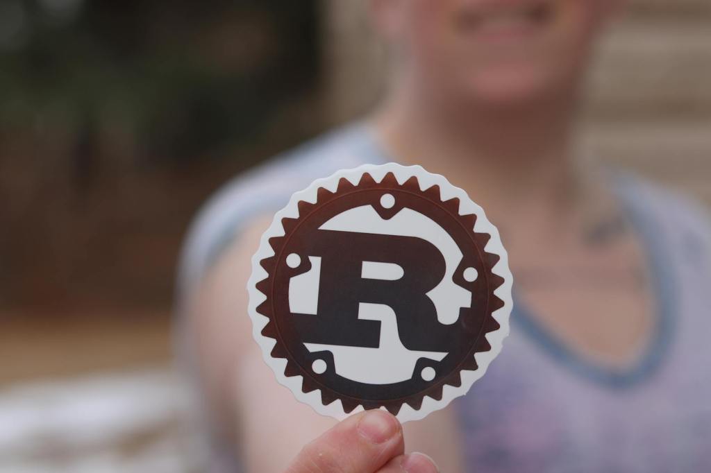 Rust Logo Sticker Being Held Up By Person in Blurred Background